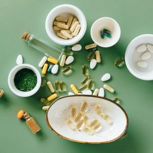 Top view of various herbal and pharmaceutical supplements in ceramic bowls on a green background.